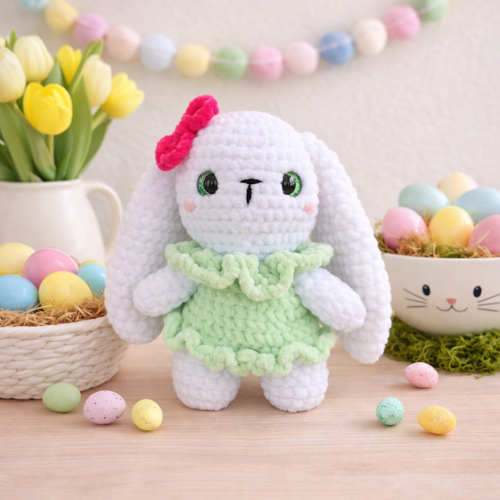 Handmade crochet bunny plush in green dress displayed with Easter eggs and spring decorations.