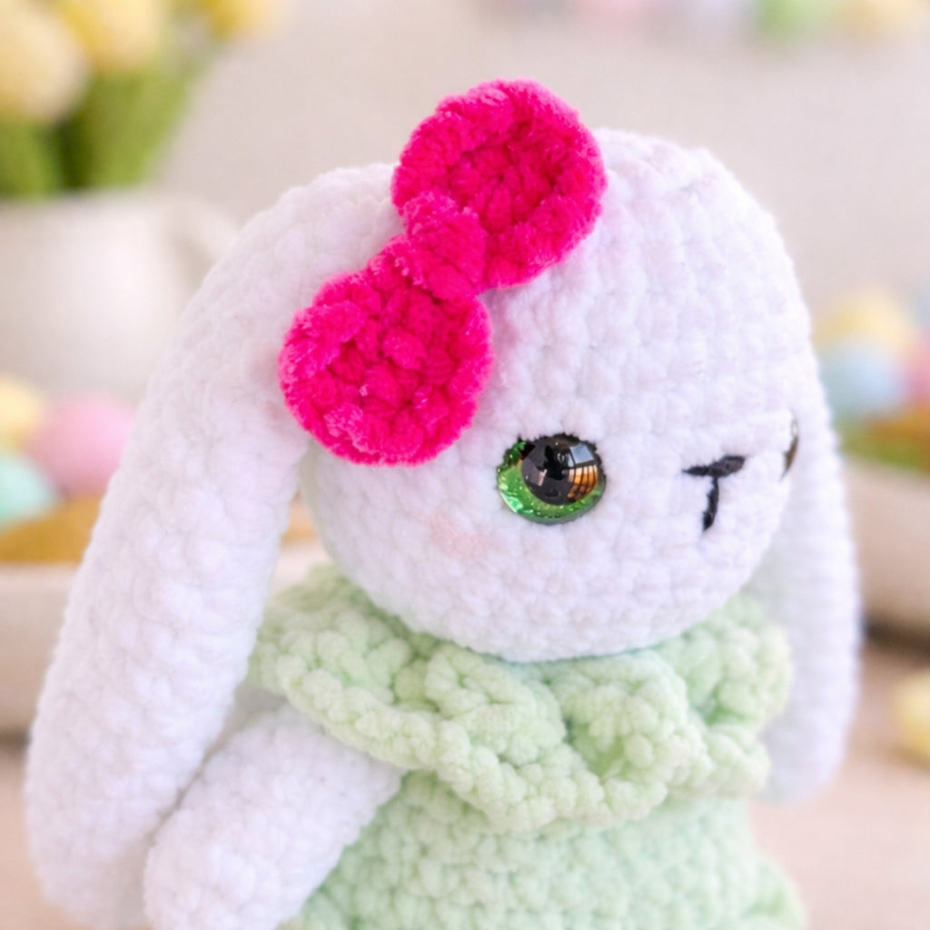Close-up of handmade crochet bunny plush with pink bow and green dress.
