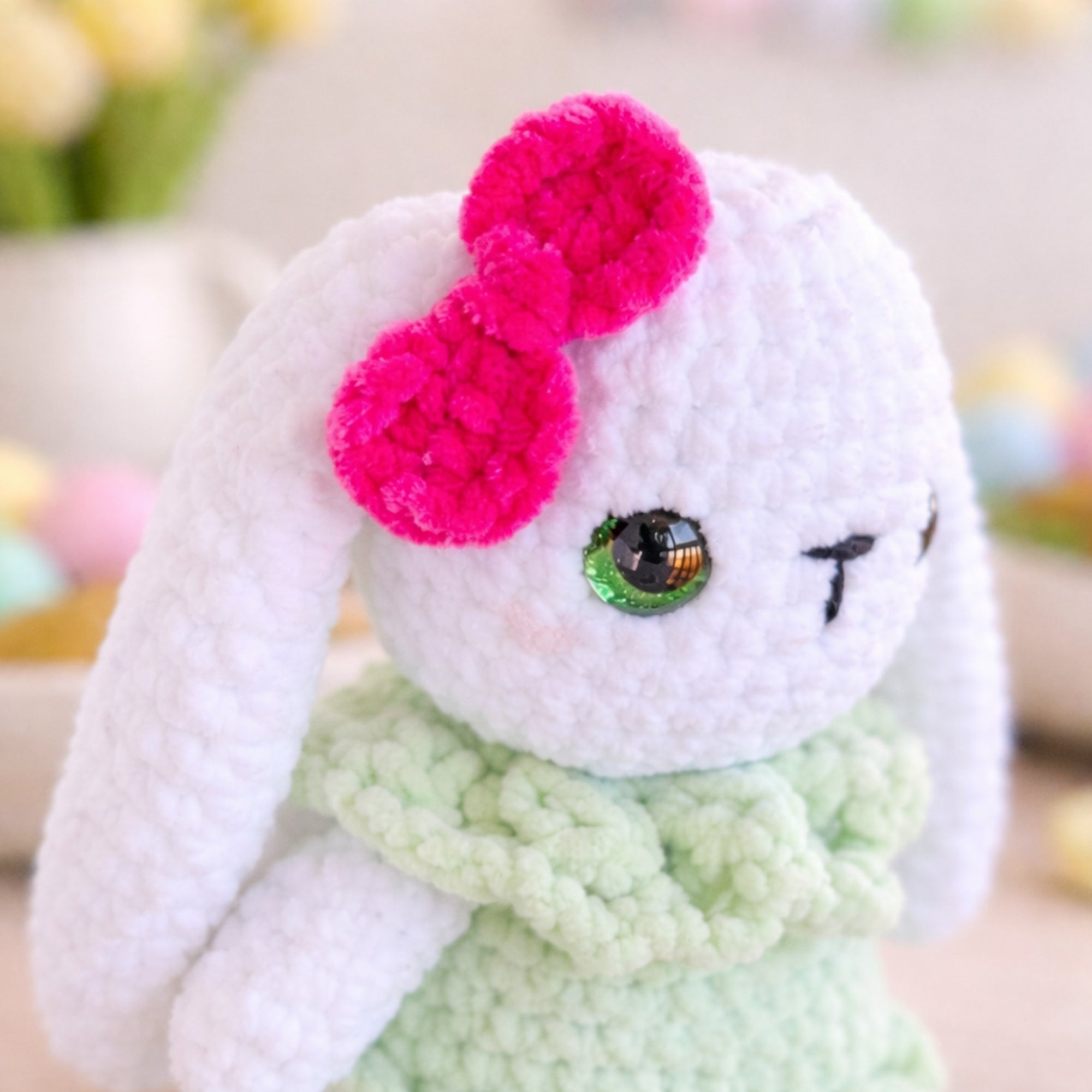 Close-up of handmade crochet bunny plush with pink bow and green dress.