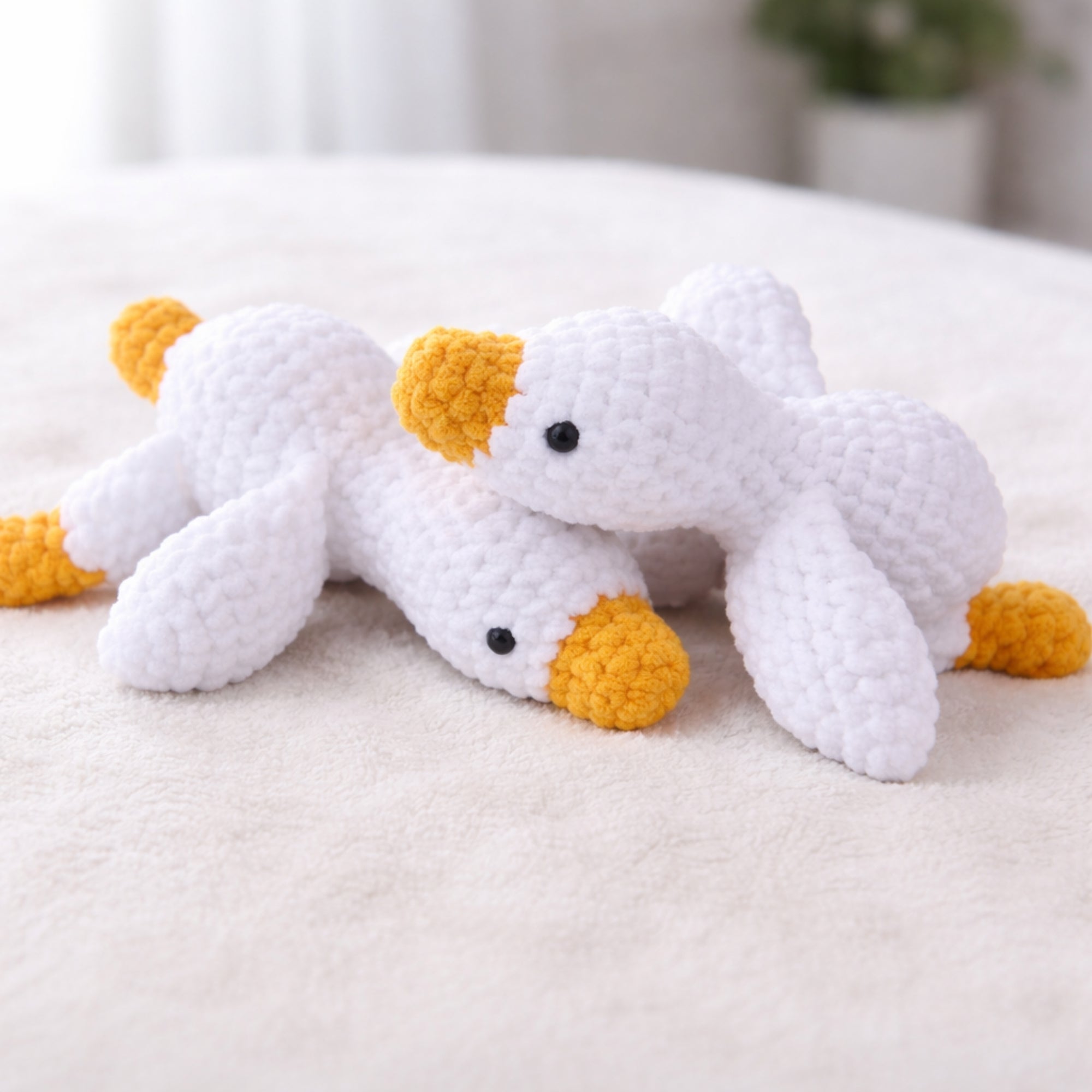 Two handmade crochet goose amigurumi plush toys on soft blanket cozy lifestyle scene