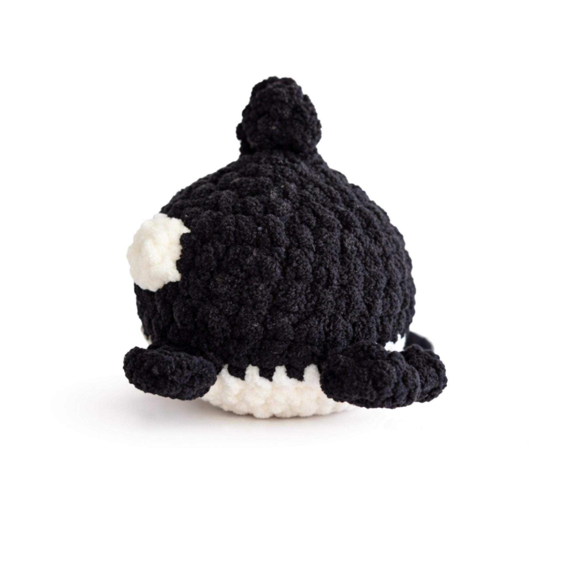 Back view of handmade crochet baby whale amigurumi plush in black chenille yarn showing tail and fins