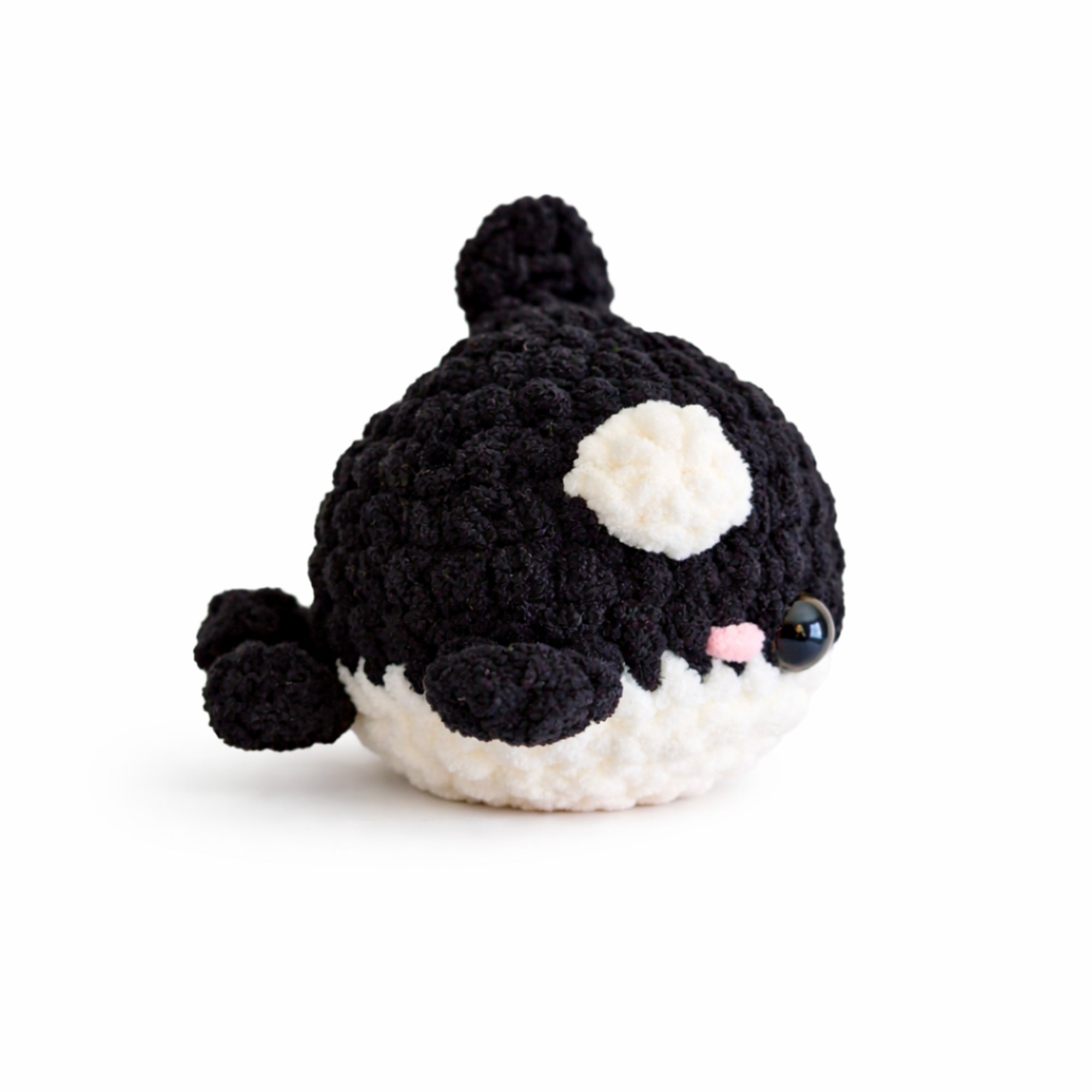 Side angle view of handmade crochet baby whale amigurumi plush in black chenille yarn showing body, fins, and tail
