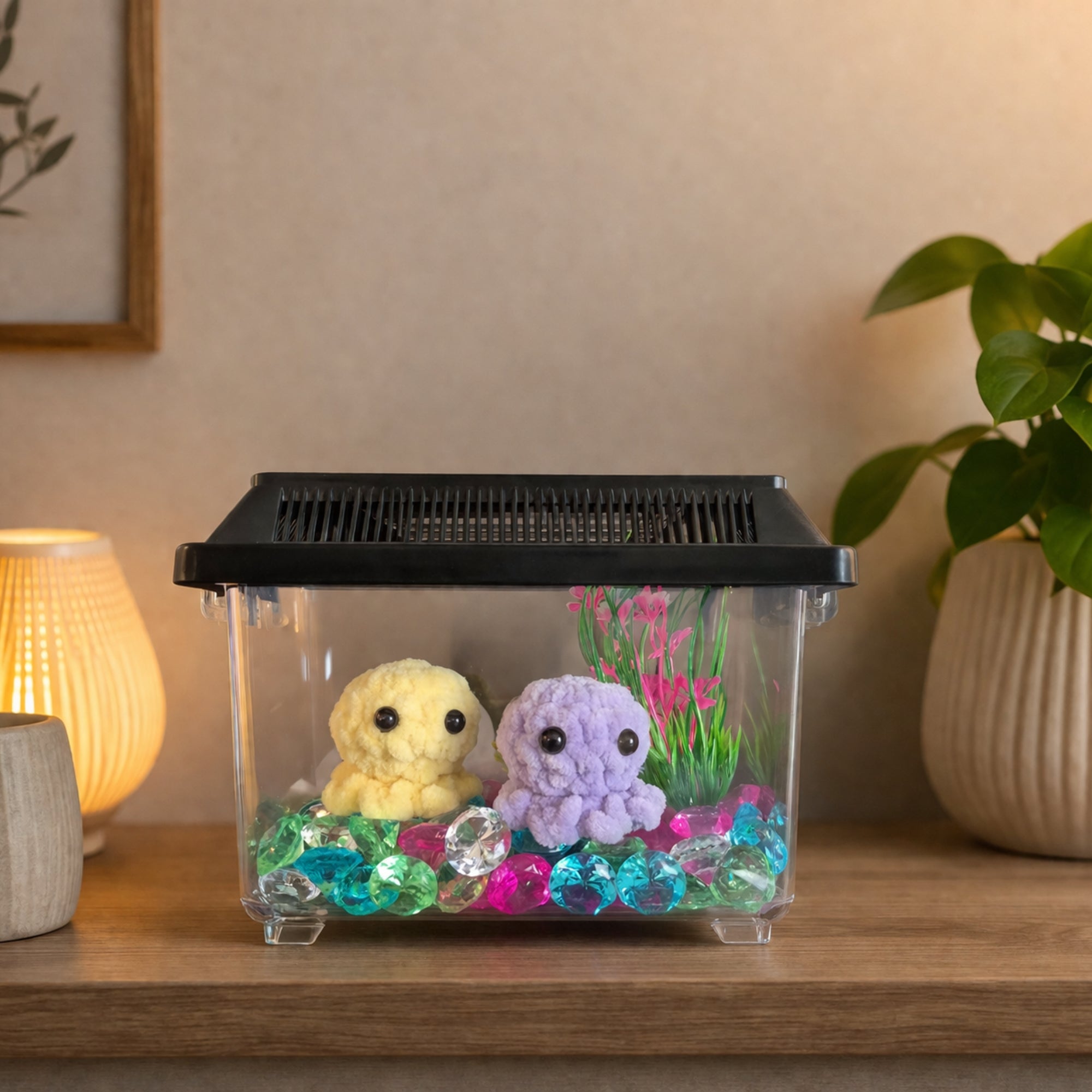 Handmade crochet octopus plush toys displayed inside a decorative aquarium with colorful gems and plants, styled as cozy home decor on a wooden table