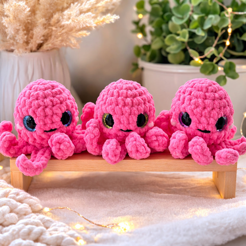 Three handmade pink crochet octopus amigurumi plush toys displayed on wooden bench with cozy decor
