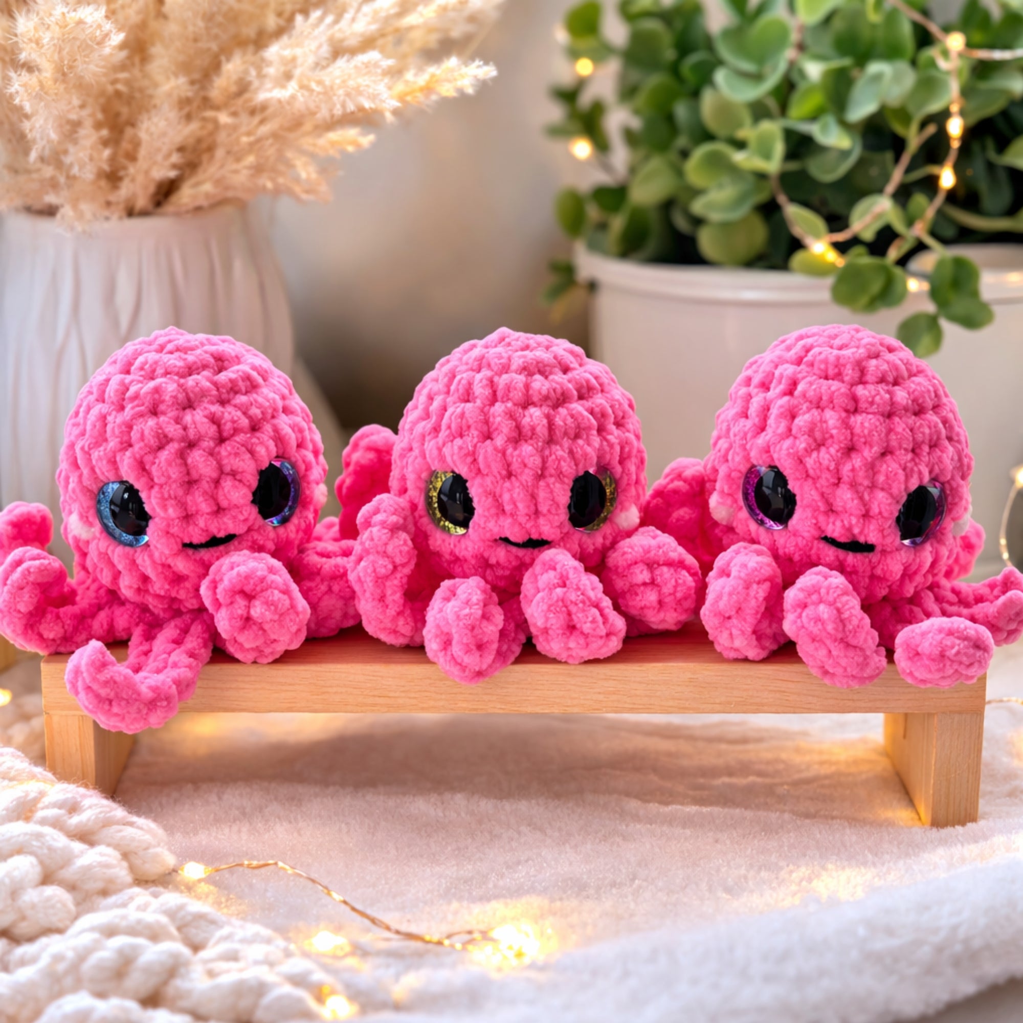 Three handmade pink crochet octopus amigurumi plush toys displayed on wooden bench with cozy decor